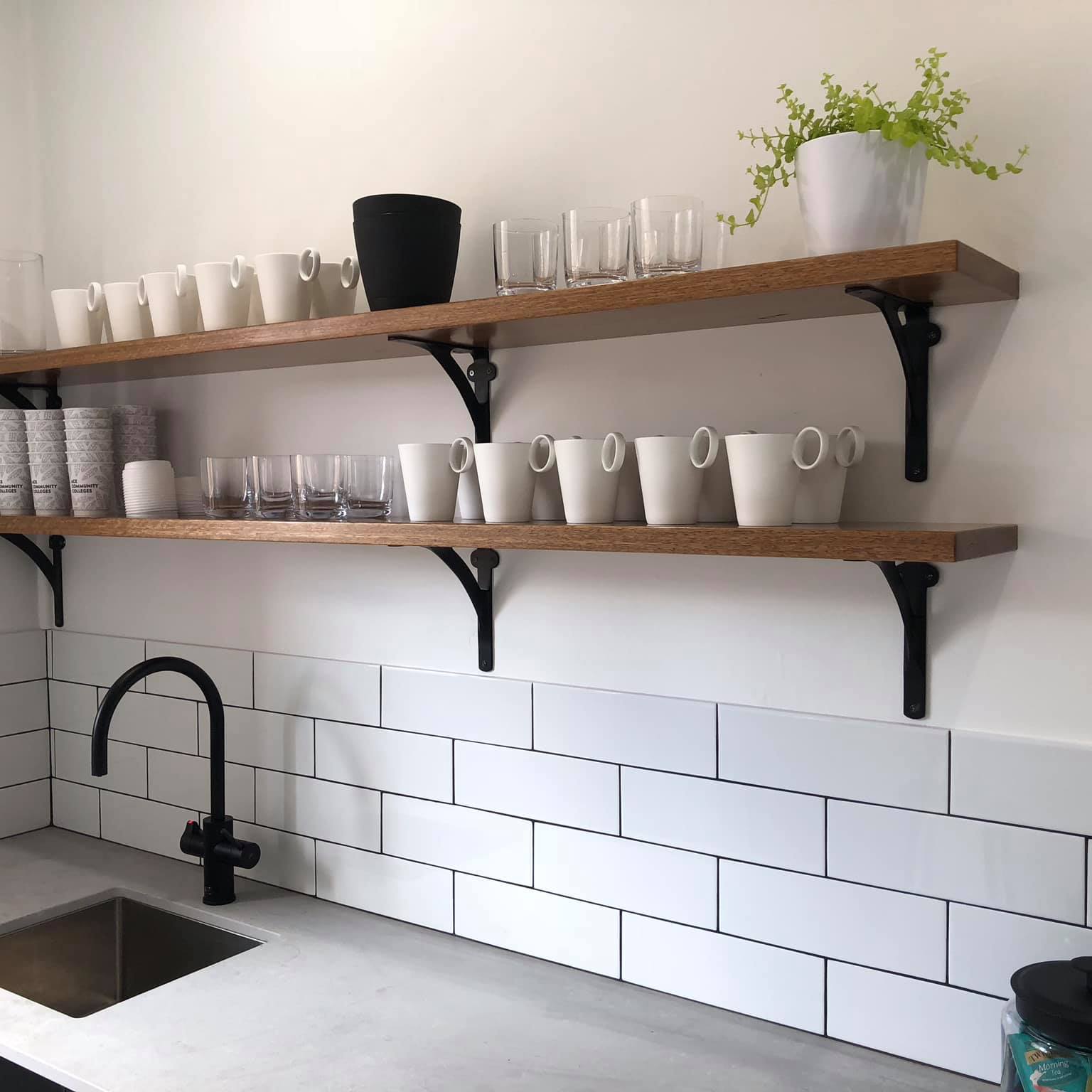 A white kitchen with subway tiles, black tapware and timber open shelving